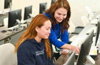 Instructor pointing at a computer screen and helping a smiling student.