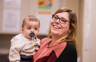 A cheerful daycare working smiling while holding an infant with a pacifier.