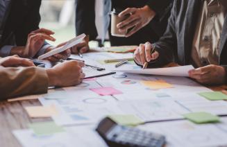 Group of colleagues collaborating on project around a boardroom table full of papers and post it notes
