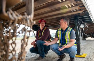 Student receiving instruction from a driving instructor underneath a semi truck