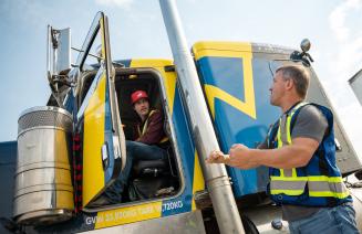 Student sitting in the cab of a semi-truck receiving instruction from a driving instructor