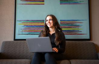 Student with a laptop sitting on a couch with a colourful painting in the background