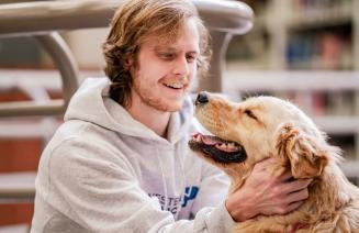 Happy student petting a therapy dog in the library