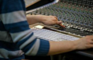  A person adjusting sliders on a mixing deck in a recording studio.