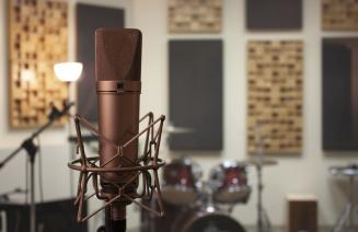 Brass coloured microphone in a recording studio with a drum set in the background