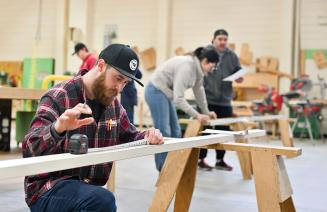 Carpentry student focused on his work in a well-equipped workshop, surrounded by tools and materials