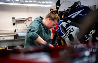 An NWP student focused on repairing a motorcycle in a well equipped workshop.