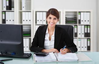 A smartly dressed professional woman smiling at her desk while working.