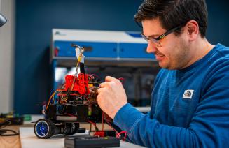A computing science student working intently on a robotic gadget in the lab.
