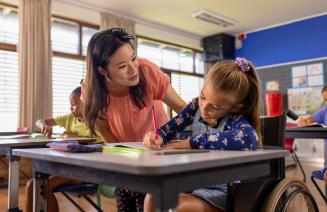 An educational assistant helping a student in a wheelchair with her writing assignment