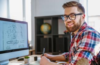 A happy engineer sitting at his computer reviewing blueprints