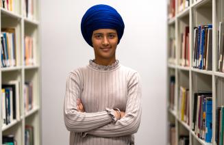 An intelligent looking woman with a blue head scarf standing in-between book shelves in a library