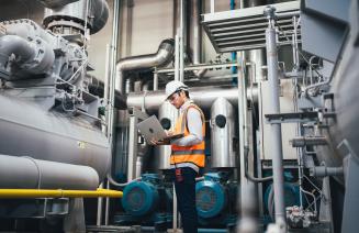 A employee in a power plant holding a clipboard and taking readings