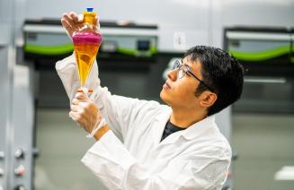 A scientist holding up and observing a separatory funnel containing pink and orange liquid.