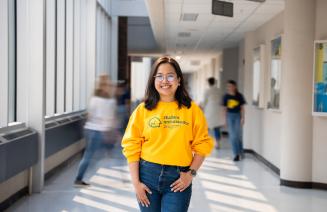 Happy student standing in a hallway on GP campus wearing a bright yellow sweatshirt 