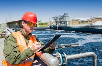 A technician with a clipboard monitoring the quality of water at a waste water treatment plant.