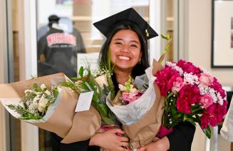Happy graduate holding bouquets of flowers and smiling broadly
