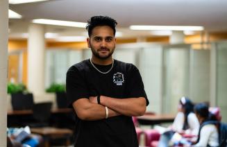 Happy student standing with arms folded in the library