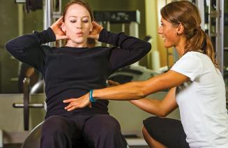 Kinesiologist observing and assisting a client who is working out with the correct exercise form