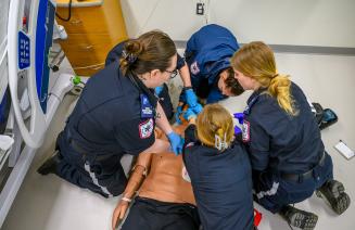 A group of paramedic students surrounding a dummy in the simulation lab