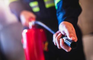 A person holding the pipe of a fire extinguisher pointing at a fire