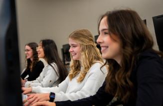 A group of students smiling and working on a project in the computer lab