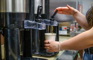 A student pours a cup of coffee from a flask in the cafeteria on Fairview campus