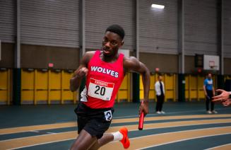 Men's wolves indoor track member running on track in race holding a baton