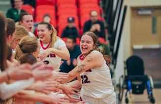Elated womens basketball player receiving multiple high fives from her team mates