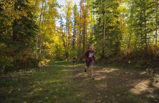 A young athlete running along a trail with trees in full fall colours in the background