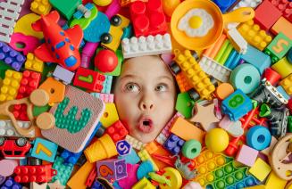 Happy child covered in colourful building blocks with only their face peeking out.