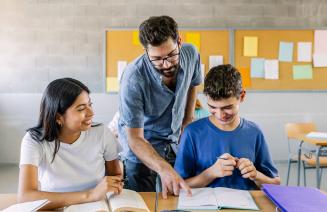 A male teacher helping two high school students on a project in a classroom