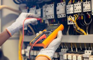 Electrician engineer uses a multimeter to test the electrical installation and power line current in an electrical system control cabinet.