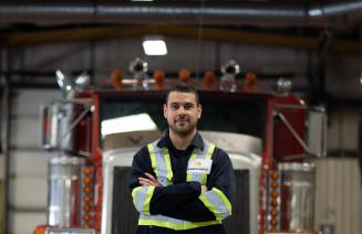 A heavy equipment technician standing with arms crossed in front of a semi truck