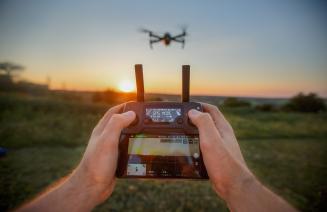 Close up of hands on a GPS remote control with a drone hovvering in the background.