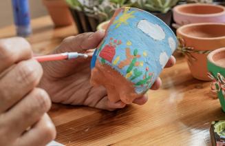 Close up shot of a person painting a colourful picture onto a clay pot