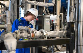 A power engineering studend wearing a hardhat and coveralls adjusts equipment in the power engineering lab