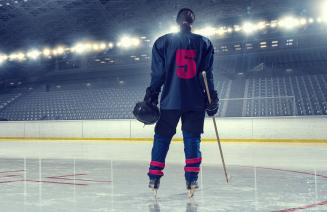 A female hockey player standing on the ice with her back to the camera displaying the number 5 on her jersey