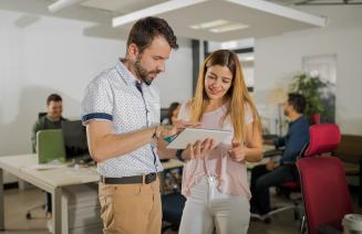 Supervisor assisting an employee in an open office with colleagues in the background