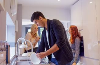 A group of happy college students laughing in the kitchen while one friend washes the dishes