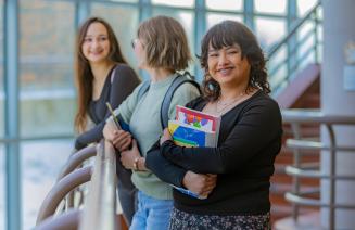 Happy student holding books and smiling as her friends socialize in the background