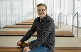 Jason Bacon, Entrepreneur in Residence sitting on a bench in brightly lit assembly hall