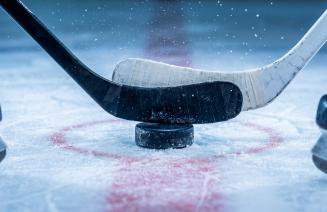 2 hockey sticks about to battle over a puck at centre ice