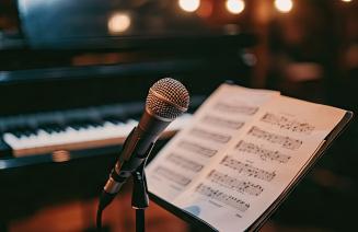  Downloaded A microphone on a stand with a sheet of music and a piano in the background, emphasizing the integration of vocal performance with musical composition.
