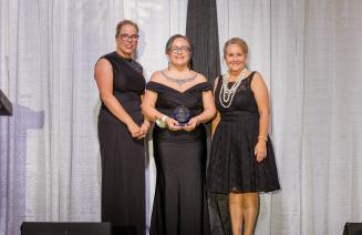 Board of Governors Award of Honour recipient Shannon Dunfield standing with her award on the stage at the President's Ball