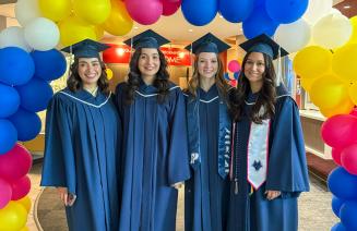 A happy group of graduates standing below a multicoloured balloon arch