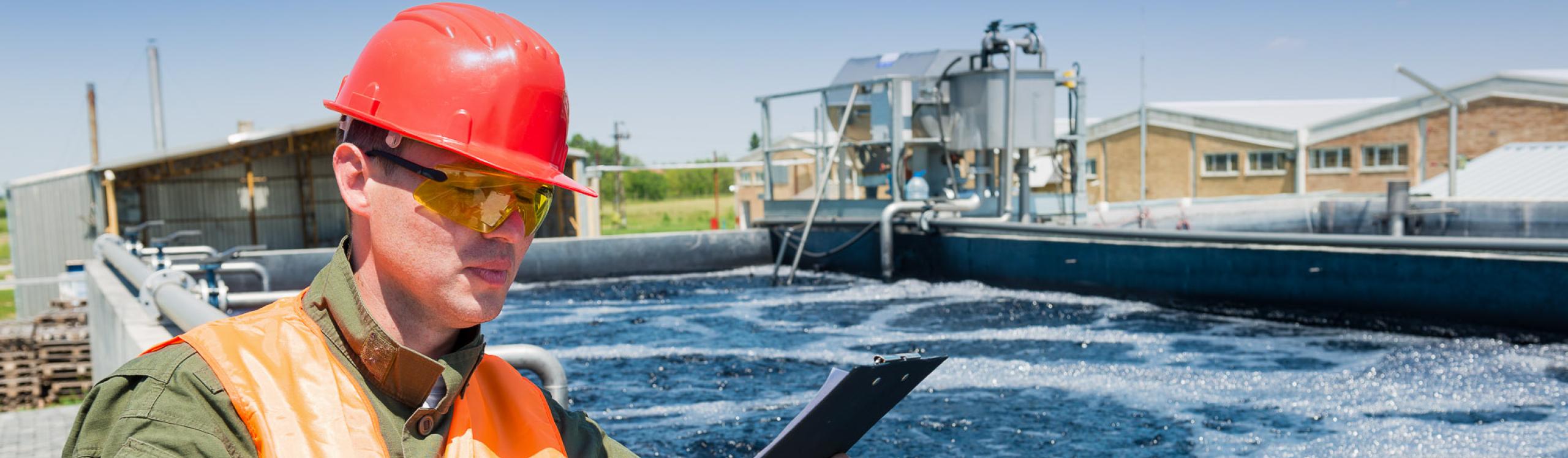 A technician with a clipboard monitoring the quality of water at a waste water treatment plant.