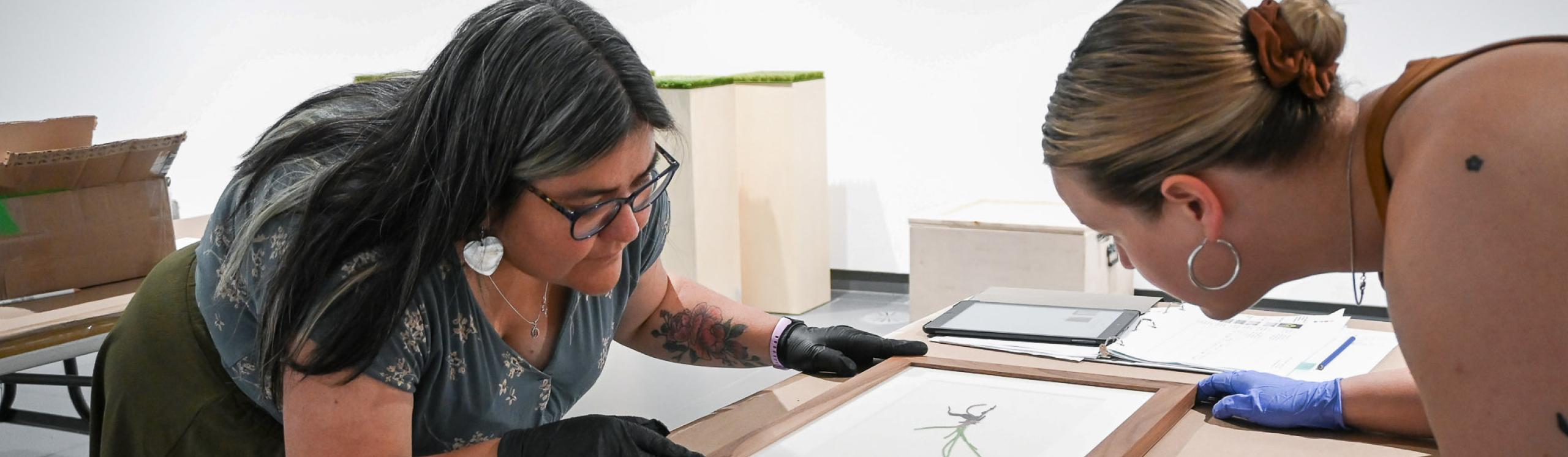 Cathy Demerais, NWP Psychology student adjusting the frame on a piece of artwork with a colleague.