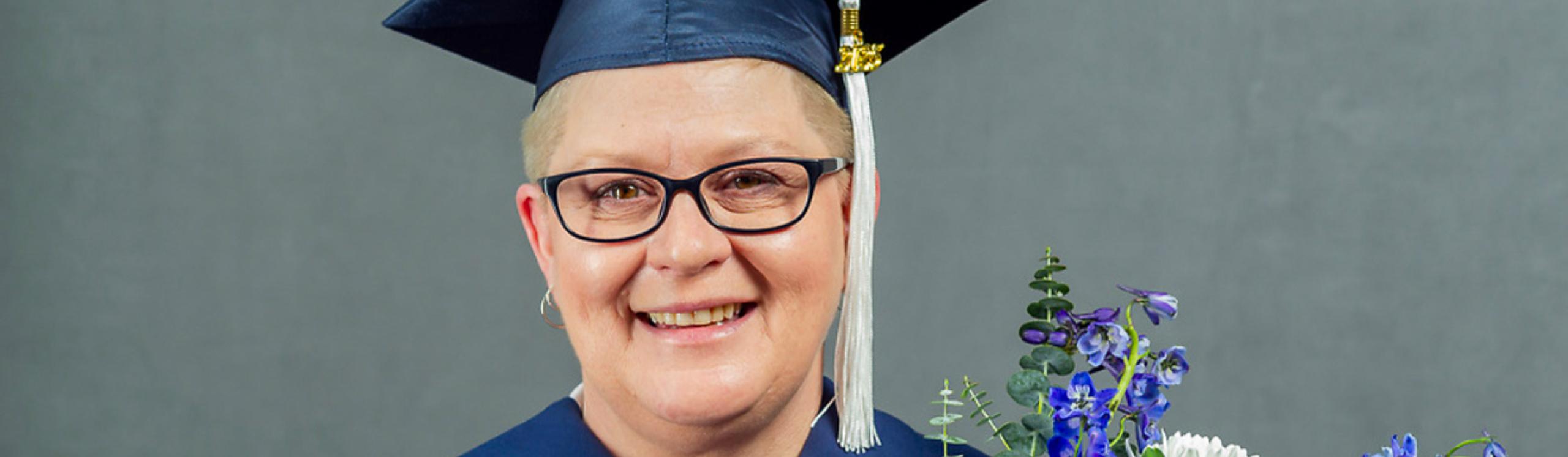 NWP Practical Nurse diploma graduate, Charity Bettenson wearing her graduation regalia and holding a bunch of flowers