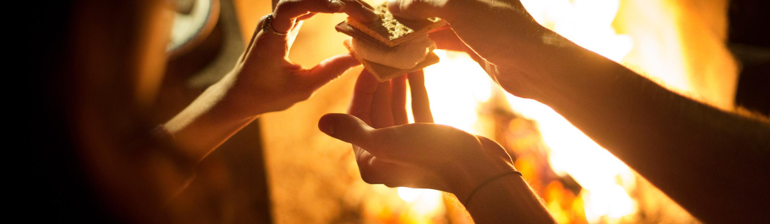 Cropped image of couple holding smores while sitting near to campfire at night